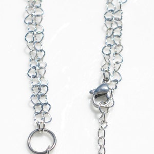 May include: A silver chain necklace with a heart-shaped link design. The necklace has a lobster clasp and a circular ring at the other end.