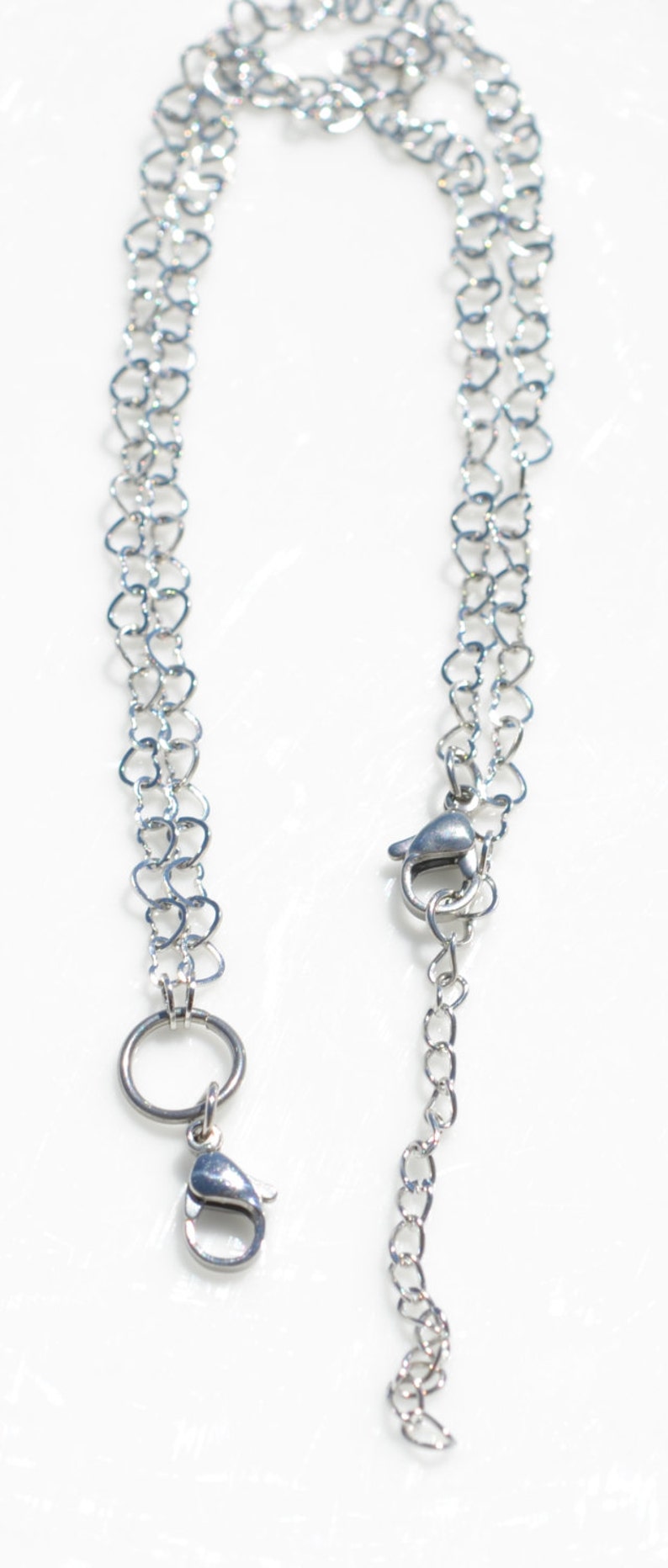 May include: A silver chain necklace with a heart-shaped link design. The necklace has a lobster clasp and a circular ring at the other end.