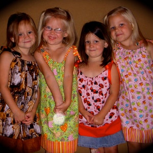 May include: Four young girls wearing colorful dresses with different patterns. The girls are smiling and looking at the camera.