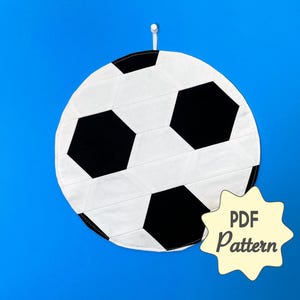 Può includere: Un'appendice da parete in tessuto a forma di pallone da calcio bianco e nero con un'etichetta di modello PDF.