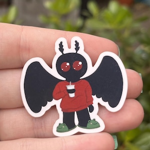 Może przedstawiać: Czarno-czerwony rysunkowy motyl w czerwonym swetrze i zielonych kapciach w kształcie żaby, trzymający kubek kawy.