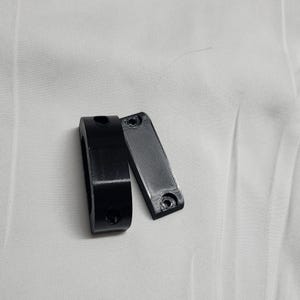 May include: Two black plastic pieces, one is a ring with two holes and the other is a flat rectangle with two holes.