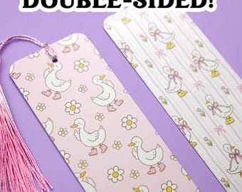 May include: Two double-sided bookmarks with a pink tassel. One bookmark features a pattern of white ducks wearing pink boots and flowers on a pink background. The other has ducks with bows on a striped background. The text "DOUBLE-SIDED!" is at the top.