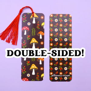 May include: Double-sided bookmark with a red tassel. One side features colorful mushrooms and floral elements on a dark background. The other side has a floral pattern. Text on the image reads "DOUBLE-SIDED!"