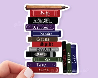 May include: A sticker featuring a stack of books with titles like "Buffy," "Angel," and "Willow." The books are in various colors, including red, black, and blue, with a pencil on top. The sticker is held by a hand.