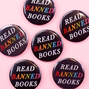 Puede incluir: Seis botones negros y blancos con el texto "Read Banned Books" en blanco. La palabra "Banned" está en colores arcoíris.