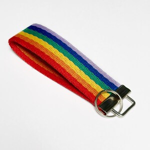 May include: A rainbow striped key chain with a silver key ring. The keychain is made of woven fabric and features the colors of the rainbow: red, orange, yellow, green, blue, indigo, and violet.