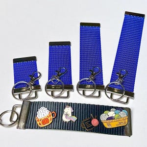 May include: Four blue keychains with silver rings and clips, and a black keychain with three enamel pins: a pumpkin spice latte, a unicorn knitting, and a coffee mug with the text "Coffee, Knit, Sleep, Repeat".