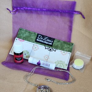 May include: A purple organza bag filled with a green and white fabric pouch, a small bottle of essential oil labeled "Christmas Spirit", a lavender lip balm, a silver locket necklace, and a small clear bag with a yellow round object.