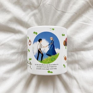 May include: A white ceramic mug featuring a circular illustration of two figures holding hands in a grassy field under a blue sky. The text reads: In the end all you can do is believe in yourself. If you don't believe in yourself, even magic won't help.