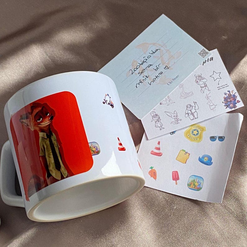 May include: A white ceramic mug featuring a graphic of a fox character in a green shirt and tie against a red background. Beside the mug are two white cards with various small stickers, including a police badge, traffic cones, and carrots.
