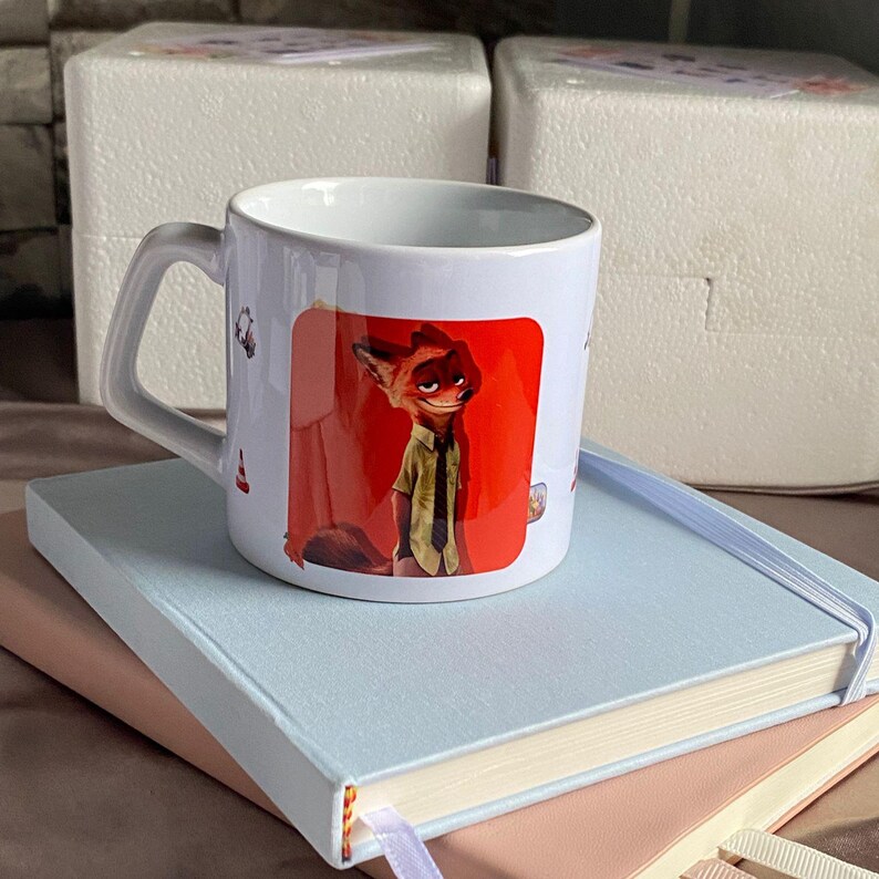 May include: A white ceramic mug featuring a graphic print of a cartoon fox character with orange fur, wearing a light green short-sleeved shirt and a dark tie, set against a vibrant red background. The mug has a curved handle and a smooth finish.