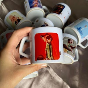 May include: A white ceramic mug featuring a graphic print of a fox character wearing a light green shirt and a dark tie against a vibrant red background. The mug has a curved handle and is part of a collection of similar mugs with various character designs.