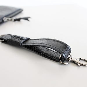 Può includere: Un portachiavi in ​​pelle nera con un anello e un gancio argentati. Il portachiavi è in pelle testurizzata e ha un design semplice.