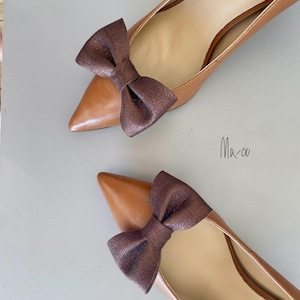May include: A pair of brown leather pumps with a pointed toe and a brown bow on the front of each shoe.