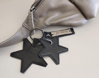 May include: A light brown leather bag with a black star-shaped keychain. The keychain has a silver ring and a silver tag that says "ma-oo".
