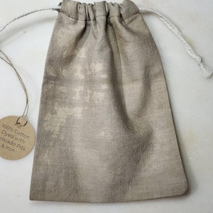 May include: A small, light brown drawstring bag made of 100% cotton. The bag is dyed with avocado pits and iron. The bag is tied with a white cord.