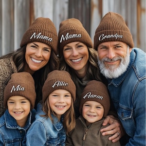 Könnte beinhalten: Eine Gruppe von Menschen trägt braune Strickmützen mit personalisierten Namen, die in Weiß gestickt sind. Die Namen auf den Mützen sind Mia, Allie, Aaron, Mama und Opa.