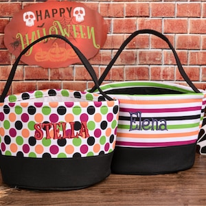 May include: Two Halloween treat bags. One bag has a black base and is covered in polka dots of green, orange, pink, and black. The name "STELLA" is embroidered in red. The other bag has a black base and horizontal stripes of green, orange, pink, and white. The name "Elena" is embroidered in blue.