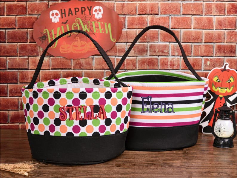 May include: Two Halloween treat bags. One bag has a black base and is covered in polka dots of green, orange, pink, and black. The name "STELLA" is embroidered in red. The other bag has a black base and horizontal stripes of green, orange, pink, and white. The name "Elena" is embroidered in blue.