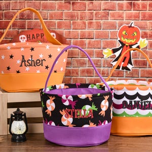 May include: Three Halloween-themed treat bags. The orange bag has black stars and the name "Asher". The black bag has candy graphics and the name "Stella". The third bag has a scalloped pattern and the name "Daniel".