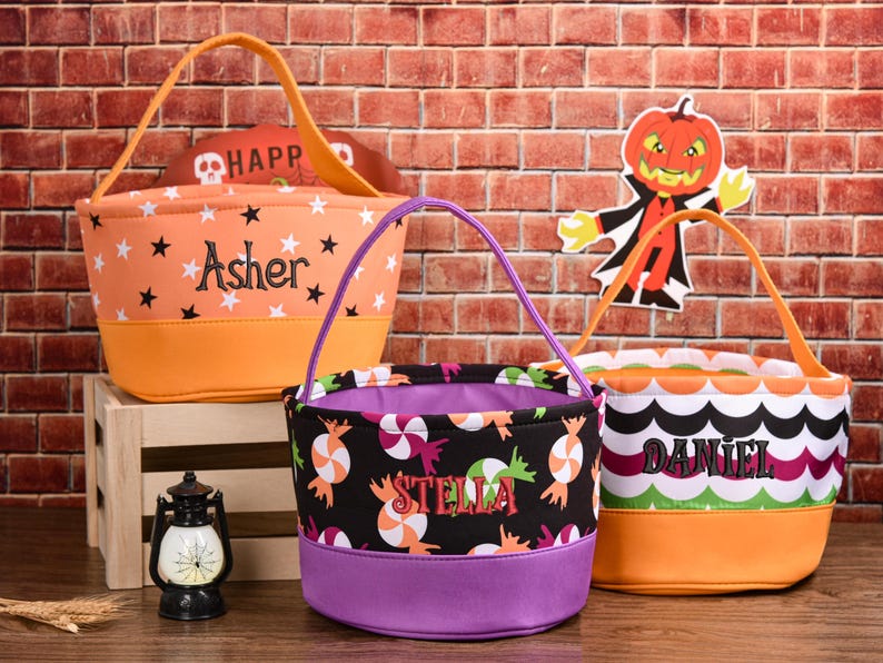 May include: Three Halloween-themed treat bags. The orange bag has black stars and the name "Asher". The black bag has candy graphics and the name "Stella". The third bag has a scalloped pattern and the name "Daniel".