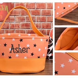 May include: Orange Halloween trick-or-treat bag with white and black star pattern. The bag has a matching orange handle and base. The name "Asher" is embroidered in black on the front. A Halloween sign is visible in the background.