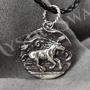 Puede incluir: Collar con colgante de plata con un dise&ntilde;o detallado de un caballo corriendo a trav&eacute;s de olas arremolinadas. El collar est&aacute; en un cord&oacute;n trenzado negro.