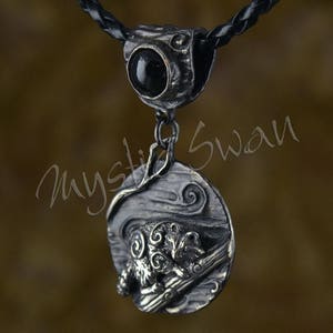 Puede incluir: Un collar de plata con un colgante de &oacute;nix negro y un dije de plata detallado de un mapache en una rama. El dije est&aacute; colocado sobre un fondo texturizado con dise&ntilde;os en espiral.