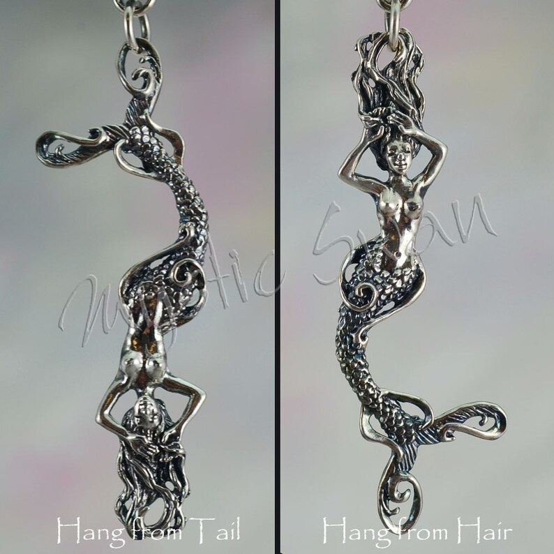 May include: Two silver mermaid pendants. One pendant shows a mermaid hanging from her tail, the other from her hair. The pendants have intricate details and the text "Hang from Tail" and "Hang from Hair". The background is a gradient of pink and white.
