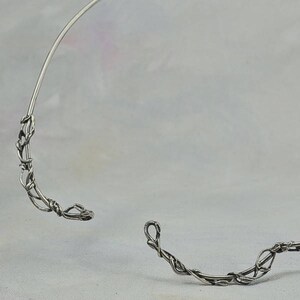 May include: A silver wire choker necklace with a delicate, vine-like design. The necklace is open in the back and has a simple, elegant style.