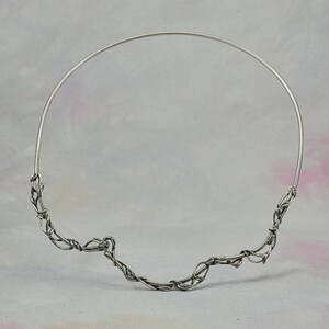 May include: A silver wire necklace with a delicate, twisted design. The necklace is made of thin wire that is twisted and woven together to create a unique and intricate pattern.
