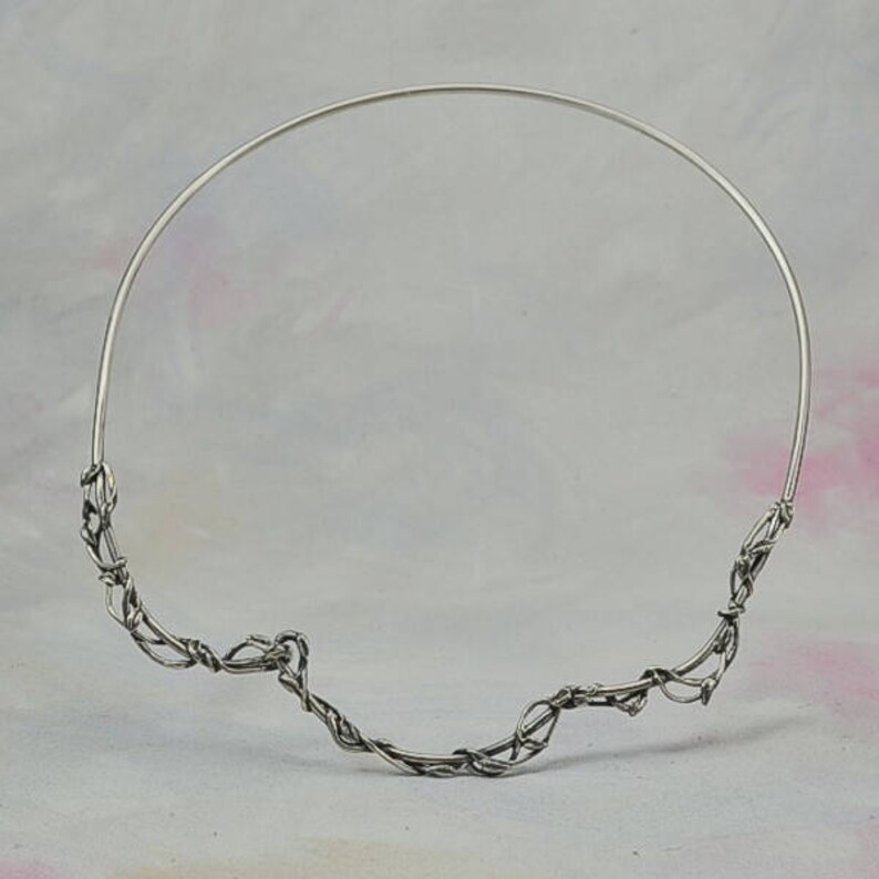 May include: A silver wire necklace with a delicate, twisted design. The necklace is made of thin wire that is twisted and woven together to create a unique and intricate pattern.