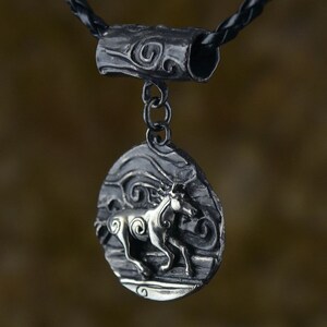 Puede incluir: Un collar con un colgante de plata de dise&ntilde;o circular que presenta un caballo estilizado corriendo a trav&eacute;s de l&iacute;neas en espiral. El colgante est&aacute; unido a un cord&oacute;n de cuero negro con un conector de barril de plata.
