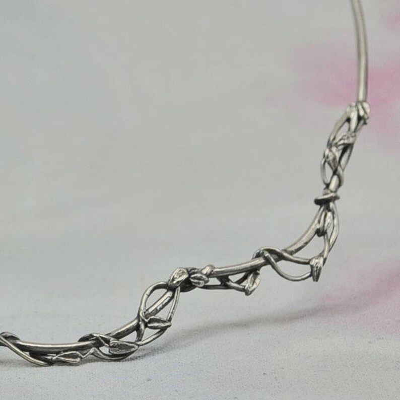 May include: Silver necklace with a delicate, intricate design of intertwining branches and leaves.