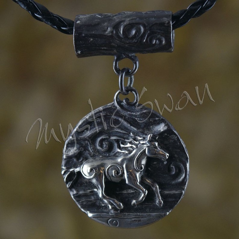 Puede incluir: Un collar con un colgante de plata en un cord&oacute;n de cuero negro. El colgante presenta un dise&ntilde;o detallado de un caballo corriendo a trav&eacute;s de un patr&oacute;n de remolino.
