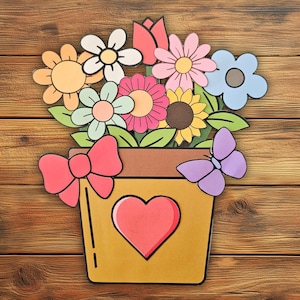 May include: A colorful paper flower arrangement in a yellow pot with a red heart. The arrangement includes various flowers, a pink bow, and a purple butterfly. The background is a wooden surface.