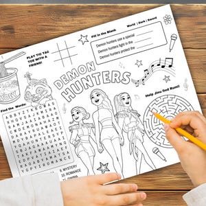 Op de afbeelding: Zwart-wit activiteitenvellen met de tekst "DEMON HUNTERS". Bevat een doolhof, woordzoeker, boter-kaas-en-eieren en invulsecties. Een hand met een gele potlood voltooit het doolhof.