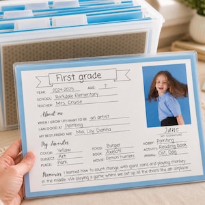 May include: A first-grade student's school form with a photo, held in front of a clear plastic storage container with blue accents. The form includes personal details, favorites, and memories. The form is in a blue frame.