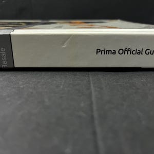 May include: A white book with the text "Prima Official Guide" printed in black. The spine has a gray label with the word "Resale" printed vertically. The book is on a dark surface.
