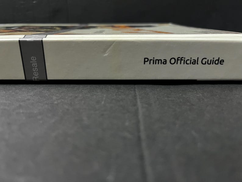May include: A white book with the text "Prima Official Guide" printed in black. The spine has a gray label with the word "Resale" printed vertically. The book is on a dark surface.
