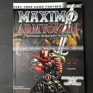 May include: A strategy guide for the video game "Maximo vs. Army of Zin." The cover features the game's title in silver and red, with a warrior holding a sword. The guide includes an exclusive art section and is published by BradyGames.
