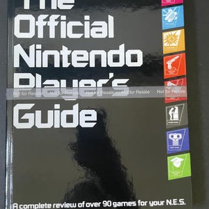 May include: Black and silver book cover with the title "The Official Nintendo Player's Guide". The cover features a variety of game icons and the text "A complete review of over 90 games for your N.E.S."