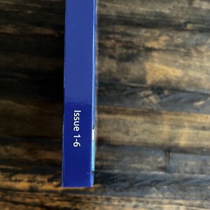 May include: A dark blue rectangular object with the text "Issue 1-6" printed in white. The object is positioned vertically against a wooden background. The object's surface is smooth.