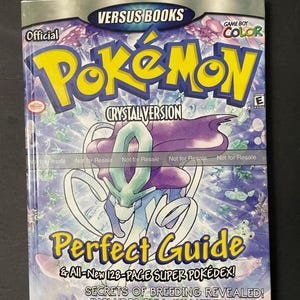 May include: A blue and purple Pokemon Crystal Version guide book with a picture of Lugia on the cover. The book is titled "Perfect Guide" and features the text "& All-New 128-Page Super Pokédex! Secrets of Breeding Revealed! Includes Full Walkthrough!"