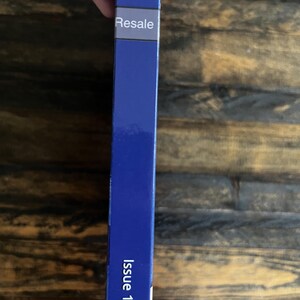 May include: A blue book spine with the word "Resale" in white text on a white label. The text "Issue 1-6" is printed in white on the lower portion of the spine. The background is a wooden surface.
