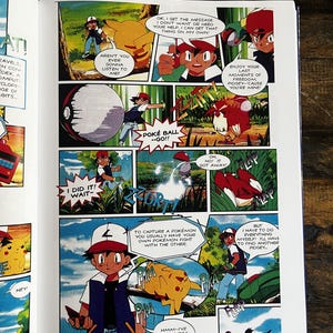 May include: A comic book page with vibrant panels from the Pok&eacute;mon series. The panels show characters like Ash and Pikachu, along with other Pok&eacute;mon, in dynamic scenes with speech bubbles. The comic book is open on a wooden surface.