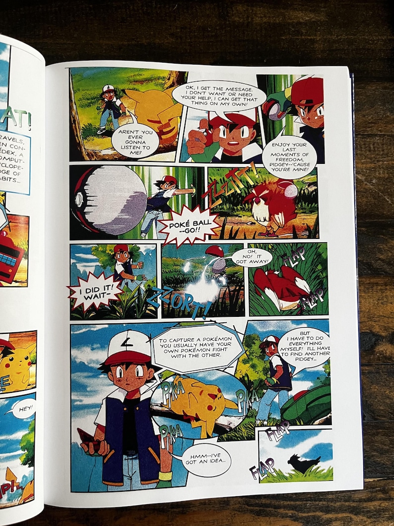 May include: A comic book page with vibrant panels from the Pok&eacute;mon series. The panels show characters like Ash and Pikachu, along with other Pok&eacute;mon, in dynamic scenes with speech bubbles. The comic book is open on a wooden surface.