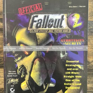 May include: The cover of the official Fallout 2 strategy guide. The cover features a futuristic helmeted face with the game's logo and the words "Strategies & Secrets." The book promises over 100 maps and essential strategies.