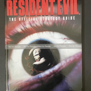 May include: A Resident Evil The Official Strategy Guide book featuring a large human eye on the cover with a zombie reflected in the pupil. The text Resident Evil, The Official Strategy Guide, Not for Resale, and Capcom are printed on the front cover.